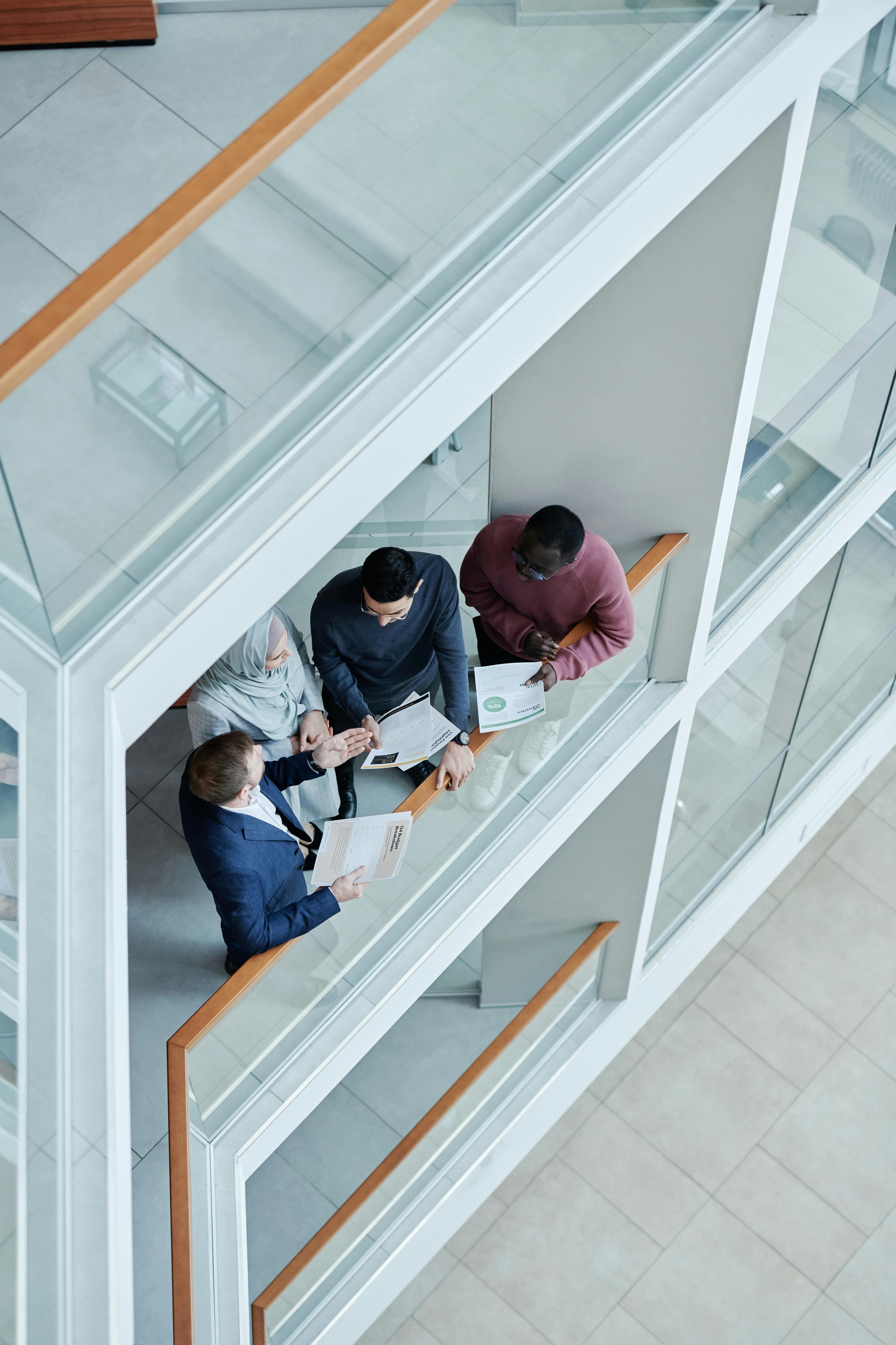 Overhead view of diverse colleagues discussing paperwork on a balcony in a bright, modern office.